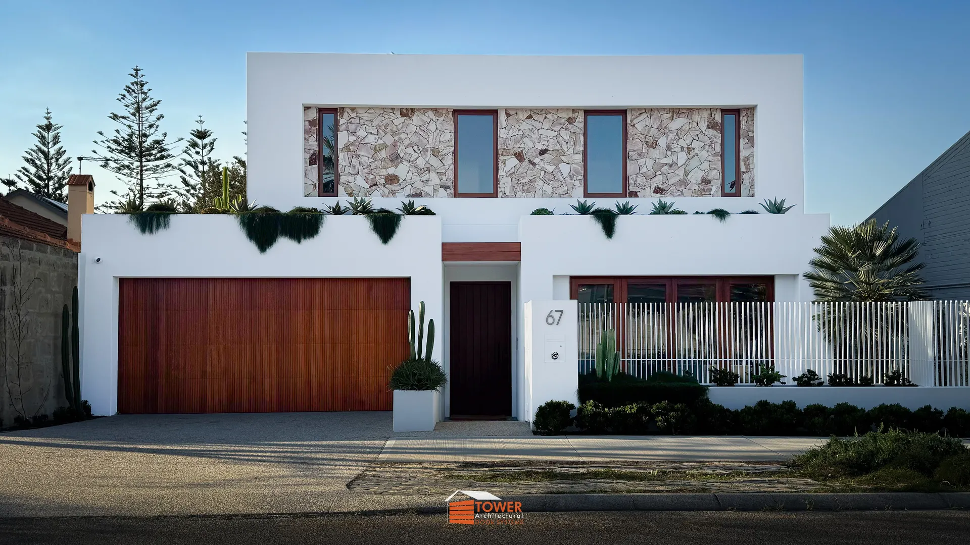 Architectural Range — Natural Series Location: Location Builder: Zorzi Style Profile: This project features a Behind Fit door clad in natural timber castellation boards, delivering a warm, textured contrast against the home’s crisp white render and stone façade.